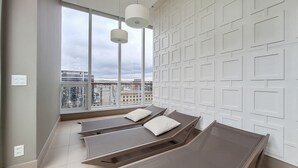 Ein Zimmer mit großem Fenster, einer weißen Wand mit geometrischem Muster und einem Bett mit zwei Kissen.