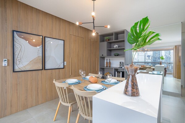 Uma sala de jantar moderna com paredes de madeira, uma mesa branca e uma grande planta verde.