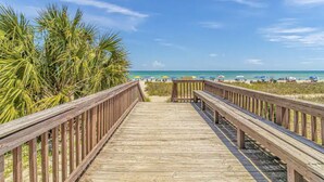 A wooden boardwalk leading to a beach with palm trees and beach umbrellas.