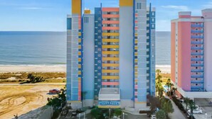 A multi-story hotel with balconies, located near a beach.