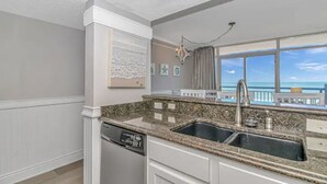 A kitchen with granite countertops, a dishwasher, and a view of the ocean through large windows.