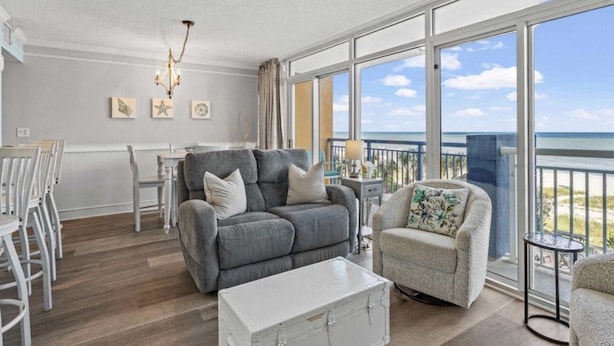 A spacious living area with a grey sofa, a white coffee table, and a balcony with a view of the ocean.