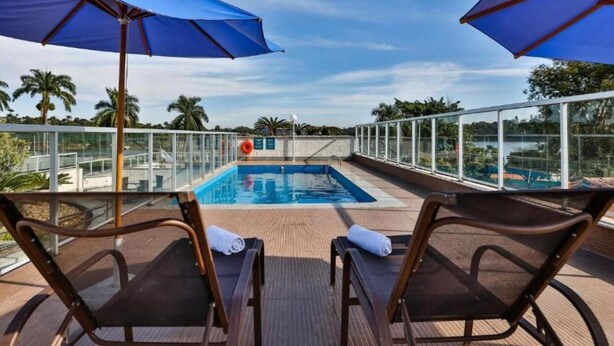 Un área junto a la piscina con dos sillones de descanso, una sombrilla azul y una barandilla de cristal con vistas a la piscina.