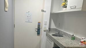 Una cocina compacta con encimera de granito, horno empotrado y un refrigerador pequeño.