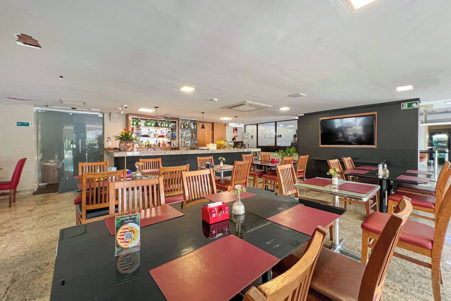Un restaurante con varias mesas y sillas, una zona de bar y una pantalla de televisión en la pared.