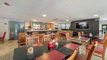 Un restaurante con varias mesas y sillas, una zona de bar y una pantalla de televisión en la pared.