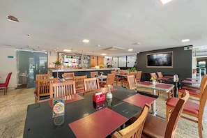Un restaurant doté de nombreuses tables et chaises, d’un bar et d’un écran de télévision fixé au mur.
