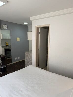 A hotel room with a bed, a bathroom, a small kitchenette, and a clock on the wall. - Suites Pampulha Hotel (Belo Horizonte)