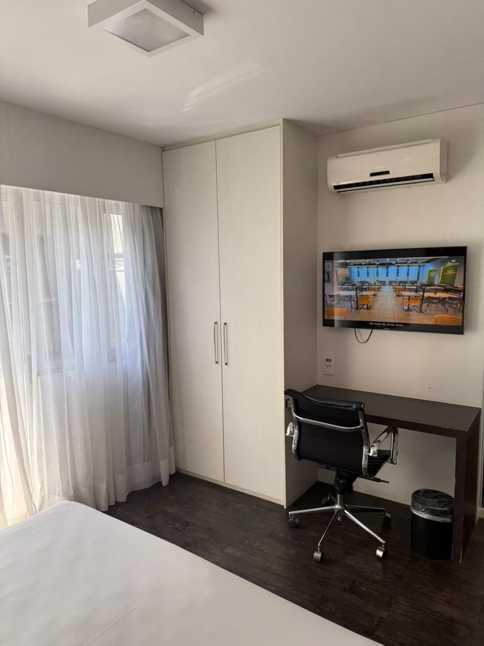 Habitación de hotel con cama, escritorio, silla, aire acondicionado, televisión y armario.
