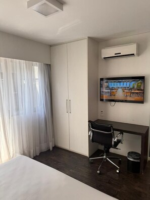 Une chambre d’hôtel équipée d’un lit, d’un bureau, d’une chaise, d’un climatiseur, d’une télévision et d’une armoire.