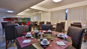 Comedor de hotel con mesas redondas, sillas y una partición de vidrio.