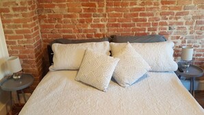 Una cama con una colcha estampada, dos almohadas y una mesita de noche con una lámpara.