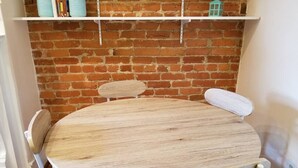 A round wooden table with four chairs, a brick wall, and a white shelf above. - Lovely, 1 BR in Adams Morgan! Walk Everywhere! (Washington)