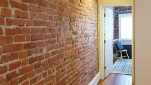 A hallway with a brick wall and wooden flooring, leading to a room with a chair and a table. - Lovely, 1 BR in Adams Morgan! Walk Everywhere! (Washington)
