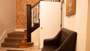 A staircase with wooden steps and a black railing, a white door, and a black leather chair in a room with a tiled floor.