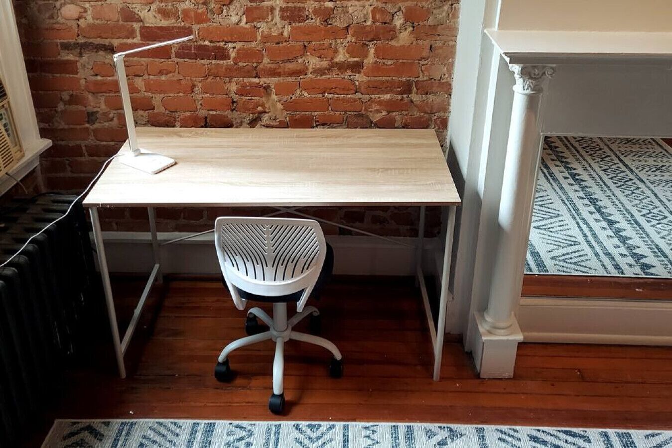 A small office space with a wooden desk, a white office chair, a radiator, and a patterned rug.