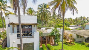 A modern two-story building with a balcony, surrounded by lush greenery and palm trees.