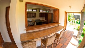 A kitchen with a bar area, wooden cabinets, and a view of the garden.