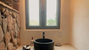 A bathroom with a stone accent wall, a window above the sink, and a dark cabinet below. - Luscious Adobe Studio in Gorgeous Abiquiu! (Abiquiu)