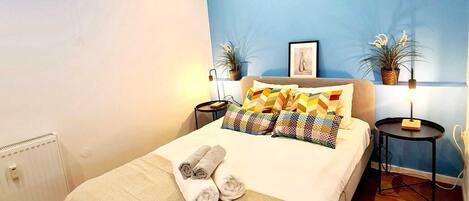 A modern bedroom with a bed, two bedside tables, a window, and a blue accent wall.
