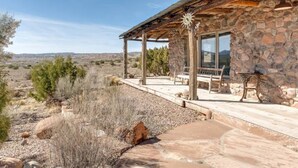 A stone building with a covered patio, outdoor seating, and a view of the surrounding landscape. - Casa Tocaya: Adobe Gem in O'Keeffe country! (Abiquiu)