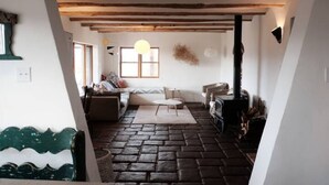 A cozy room with a stone floor, a sofa, a table, and a fireplace. - Casa Tocaya: Adobe Gem in O'Keeffe country! (Abiquiu)