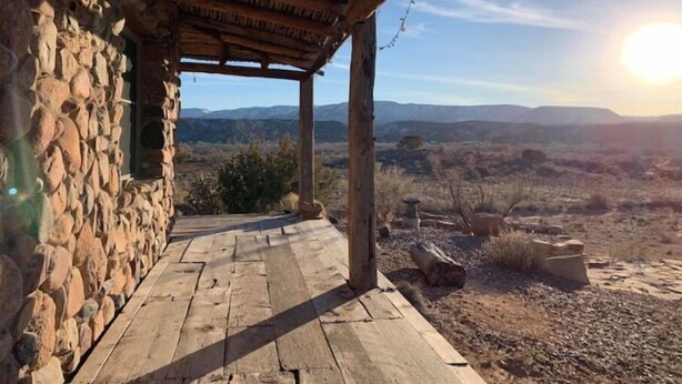 A stone building with a wooden porch leading to a scenic view. - Casa Tocaya: Adobe Gem in O'Keeffe country! (Abiquiu)