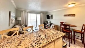 A kitchen with a granite countertop, wooden chairs, a dining table, and a TV mounted on the wall. - Coastal Condo - Beach view, resort (Galveston)