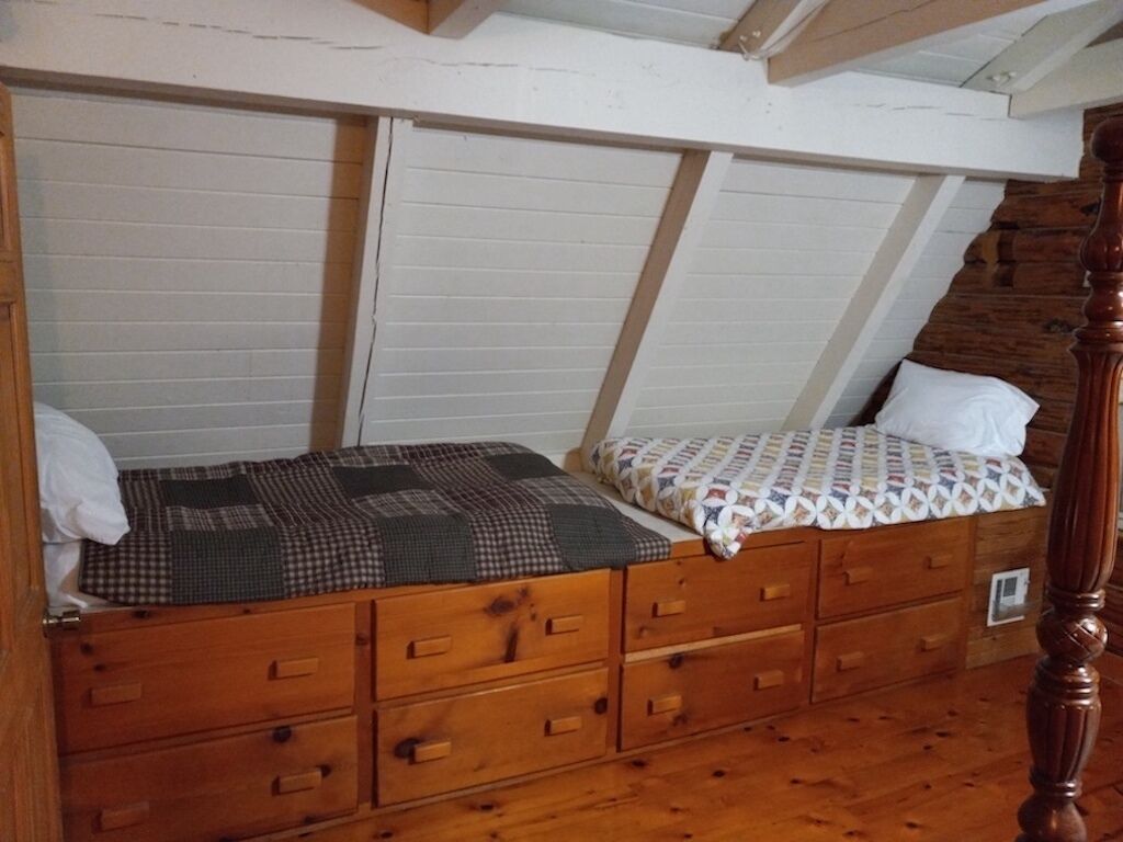 A bedroom with a loft bed, wooden drawers, and a sloped ceiling.