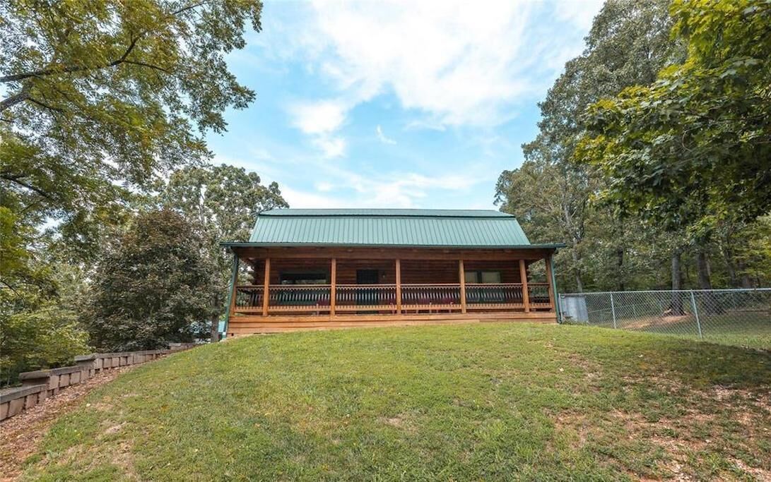 A wooden cabin with a green roof, surrounded by trees and a grassy area.
