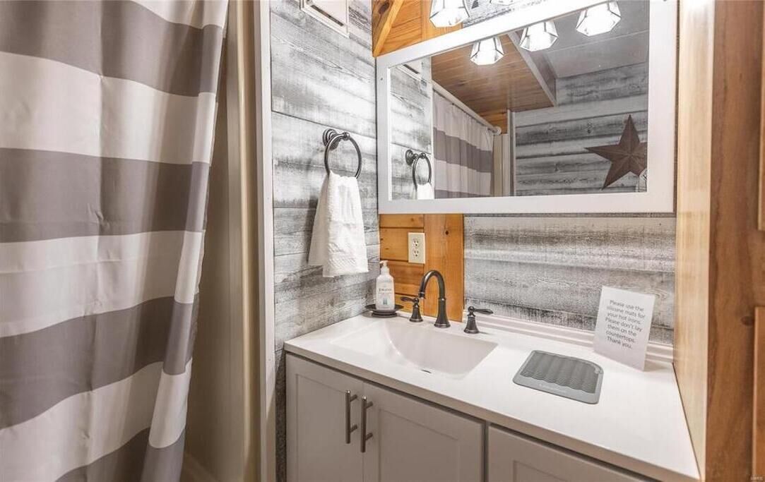 A bathroom with a white sink, a mirror, a towel ring, and a wooden accent wall.