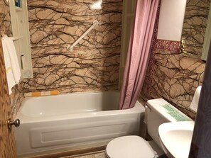 A bathroom with a bathtub, toilet, and a marble-patterned wall.