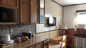A kitchen with wooden cabinets, a tiled backsplash, a microwave, a television, and a small dining area. - Heritage place Hotel  (Gravelbourg)