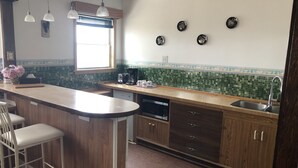 A kitchen with a wooden countertop, a sink, and a microwave. There are three bar stools and a window with blinds. - Heritage place Hotel  (Gravelbourg)