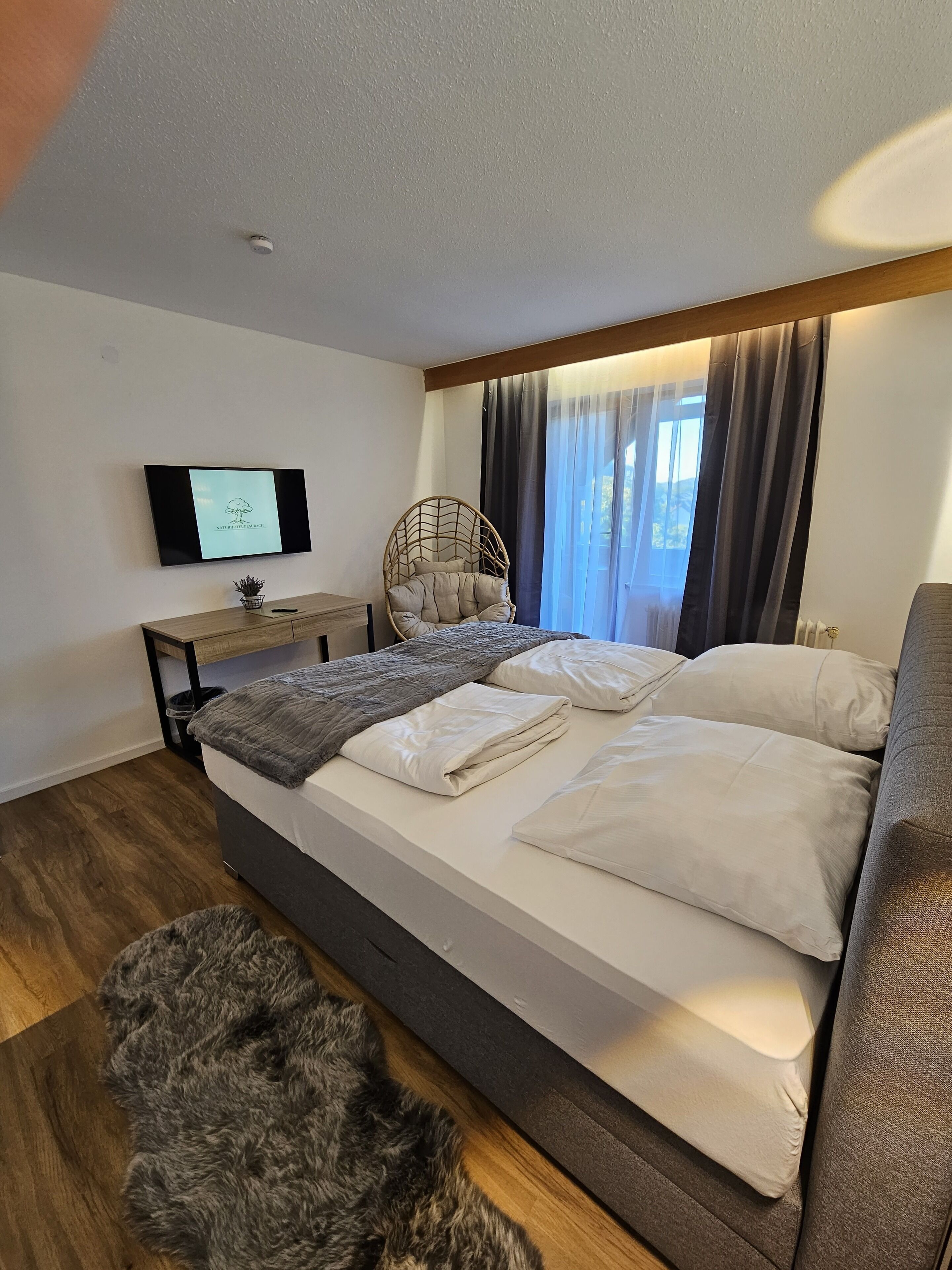 A modern bedroom with a bed, a TV, a chair, and a window with curtains.