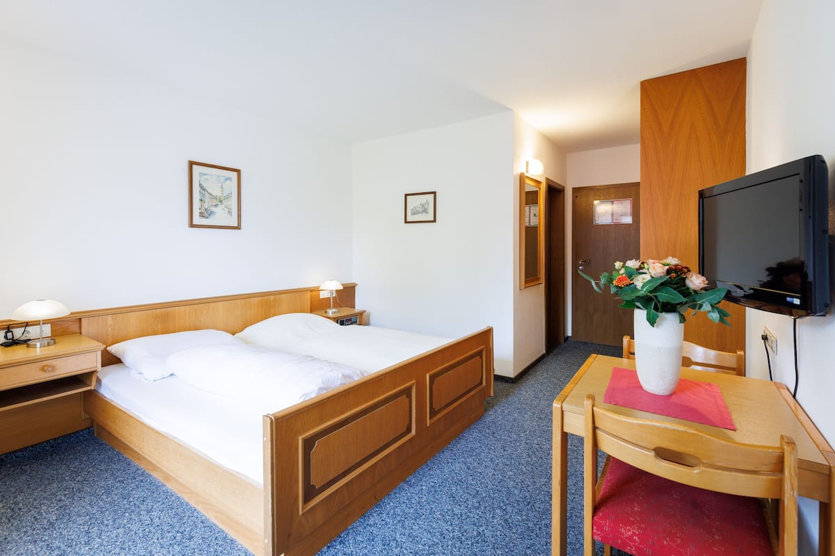 Een hotelkamer met een houten bed, een bureau met stoel, een televisie en een vaas met bloemen.