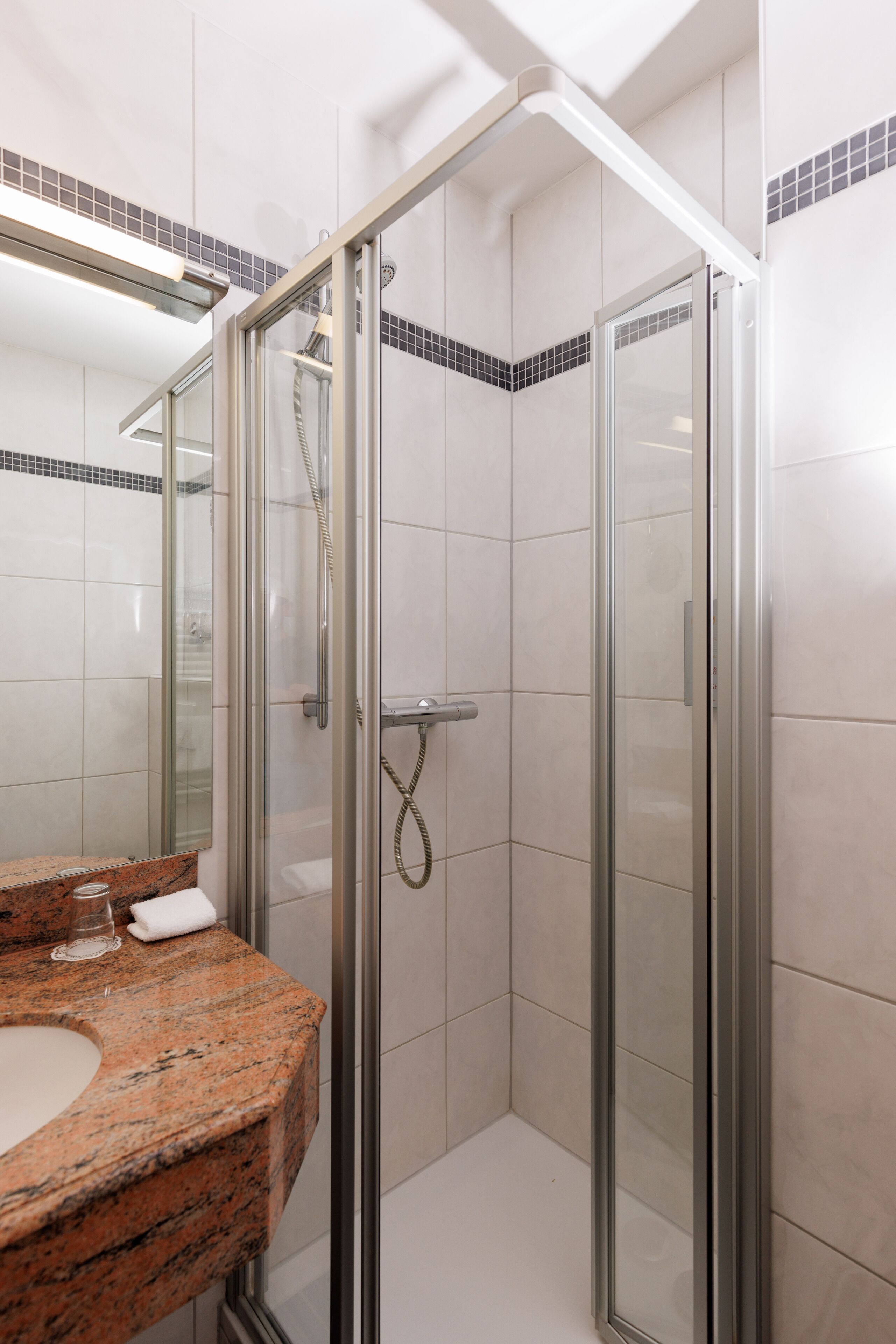 Une salle de bain moderne avec une douche à parois de verre, un comptoir en granit et un miroir au-dessus du lavabo.