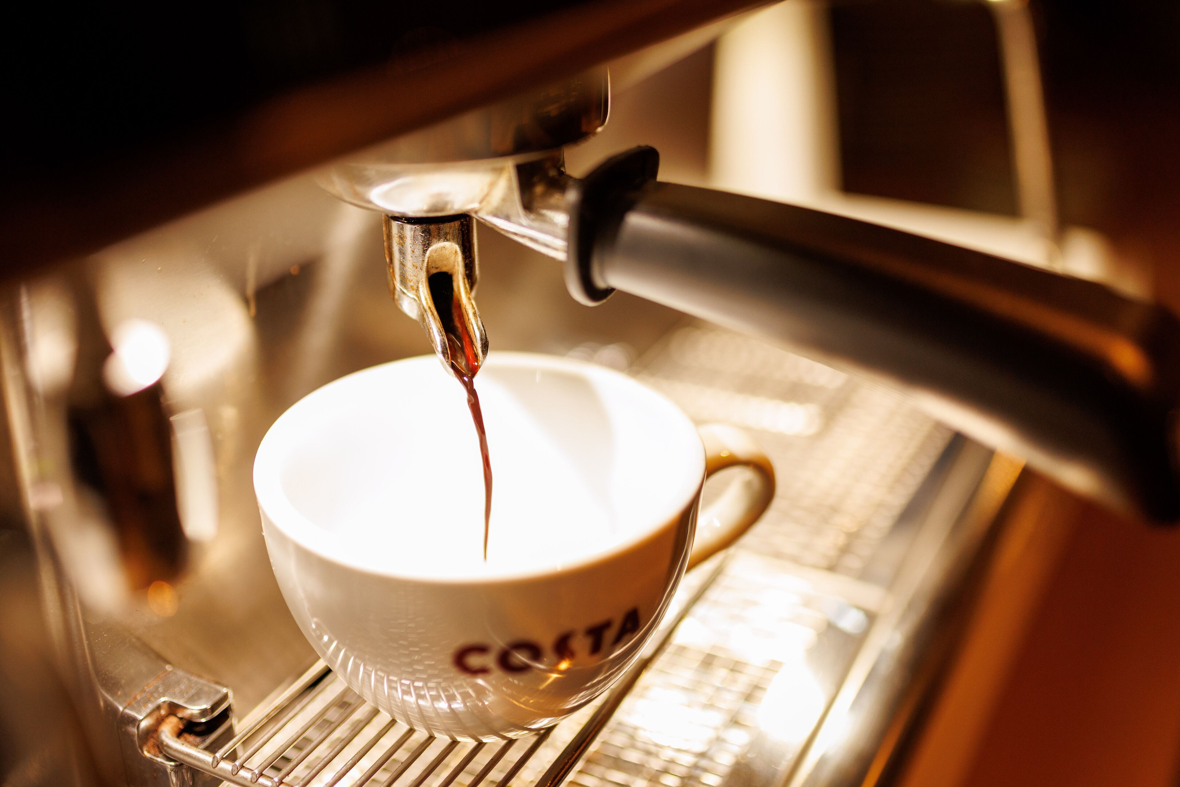 A coffee machine dispensing espresso into a cup labeled "COSTA."