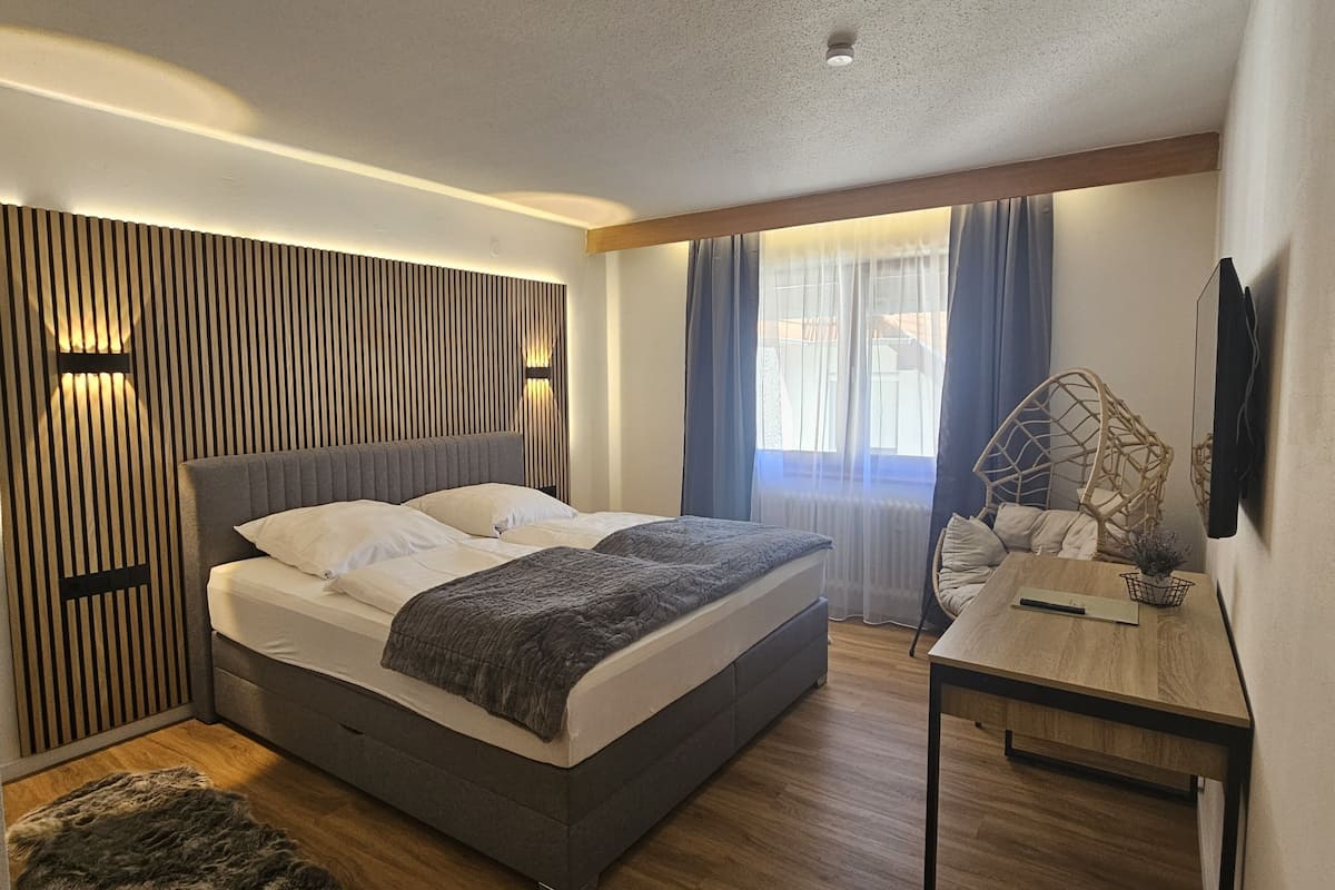 Een moderne slaapkamer met een groot bed, een houten bureau en een decoratief wandpaneel.