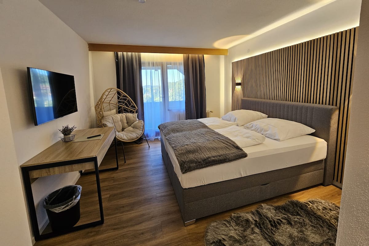 Een moderne slaapkamer met een groot bed, een bureau met stoel, een televisie en een raam met gordijnen.