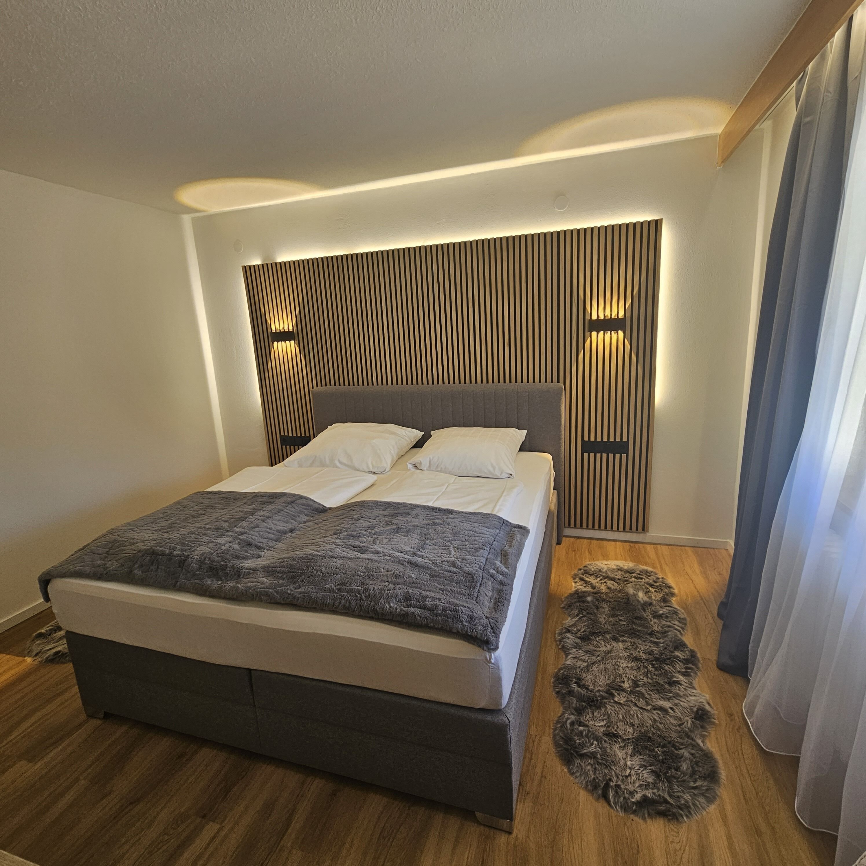 A modern bedroom with a large bed, a wooden slat headboard, and a fluffy rug.
