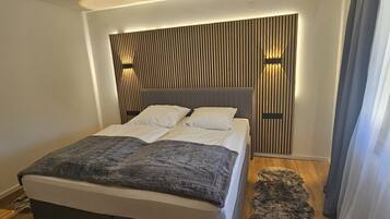 Een moderne slaapkamer met een groot bed, een hoofdbord van houten latten en een pluizig vloerkleed.