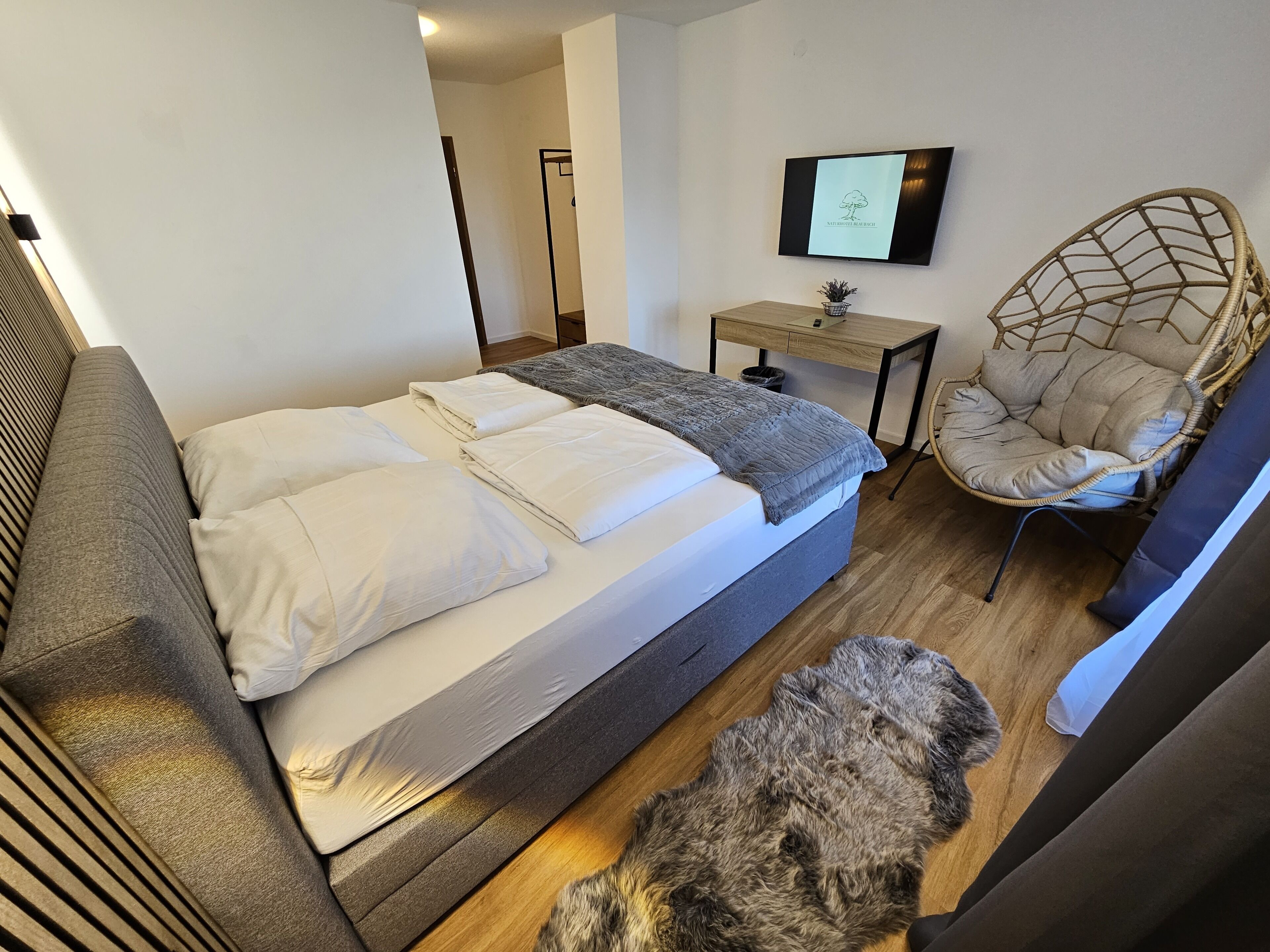 A bedroom with a bed, a chair, a desk, and a television.