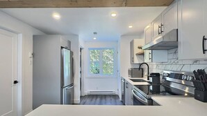 A modern kitchen with white cabinetry, stainless steel appliances, and a window providing natural light.