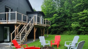 A house with a deck, outdoor seating area with Adirondack chairs, and a fire pit.