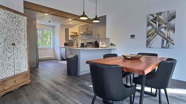 A modern kitchen with a central island, pendant lighting, and a dining area with a wooden table and black chairs.