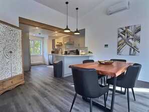 Una cocina moderna con una isla central, iluminación colgante y un comedor con mesa de madera y sillas negras.