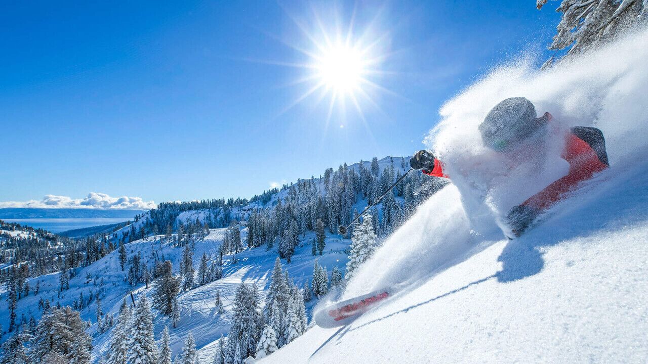 A skier in motion on a snowy slope with a clear sky and distant mountains.