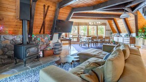 Una sala de estar acogedora con chimenea de piedra, vigas de madera, un sofá y un comedor con luz natural.