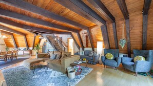 Un loft espacioso con vigas de madera a la vista, una escalera, un sofá, sillones y un comedor.